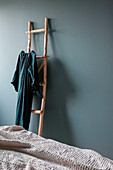 Wooden ladder with dress on hanger in bedroom with grey-blue wall