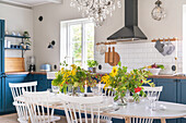Hell eingerichtete Küche, blauen Fronten und weißem Tisch mit frischen Blumen