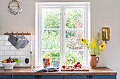 Kitchen window with view of the greenery, vases with sunflowers and fresh fruit