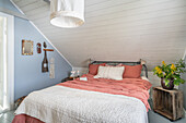 Schlafzimmer mit Dachschräge, Metallbett und sommerlicher Bettwäsche in Apricot