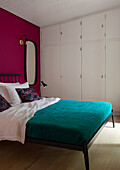 Bedroom with bed, dark teal blanket, built-in wardrobe and walls in magenta