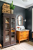 Antique wooden furniture in bathroom with dark walls and houseplant