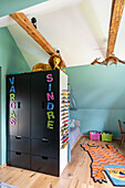 Kinderzimmer mit Dachschräge, schwarzem Schrank, buntem Teppich und Spielzeugaufbewahrung