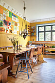 Langer Holztisch mit Stühlen im Essbereich mit gelben Wänden und Fensterblick