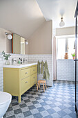 Bathroom with yellow washbasin, chequered floor and wooden stool