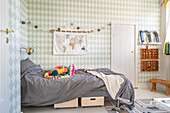 Wallpaper with diamond pattern, bed with colourful cuddly snake and play rug in children's room