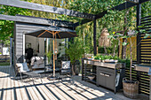 Terrasse mit Liegestühlen, Sonnenschirm und Outdoor-Küche im Sommer