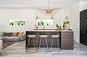 Open-plan kitchen with counter, bar stools and pendant light in modern style