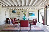 Dining room with rustic stone wall and red chairs at a wooden table