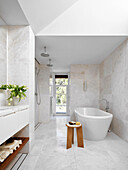 Freestanding bath and rain shower in light bathroom with marble floor tiles