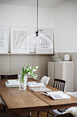 Books and white tulips on a wooden table, hanging lamp above, drawings on a narrow shelf