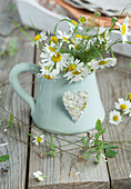 Bouquet of camomile in a jug, decorated with a heart of camomile blossoms, with strawberry vines
