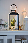 Lantern with lights and fir branches on a white sideboard with glass doors