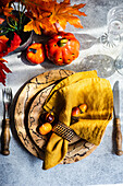 Gedeck mit Stoffserviette auf herbstlich dekoriertem Tisch mit Blättern und Kürbissen