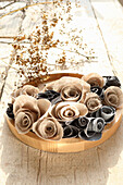 Beige and grey fabric roses on round wooden plate, dried grass in the background
