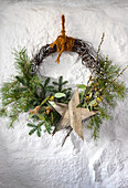 Weihnachtlicher Kranz mit Tannenzweigen und Holzstern an weißer Wand