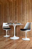 Gedeckter Tisch mit modernen Stühlen vor Holzpaneelen