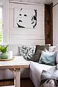 Sofa mit Dekokissen, Holztisch, holzvertäfelte Wand mit Porträtbild