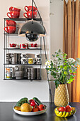 Obst-Gemüse-Schale und Blume auf Küchentheke, im Hintergrund Wandregal mit Geschirr