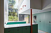 Maßgefertigte Küche mit grünen Fronten in hohem Raum mit Gartenblick