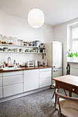 A white kitchenette with a wooden work surface, shelves and a fridge