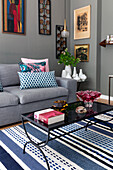 Grey upholstered sofa with throw pillows and a coffee table on a blue and white striped rug