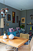 Table with chairs, in the background grey upholstered sofa with throw pillows and artwork on grey wall