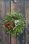 Wreath made of mistletoe with velvet ribbon, rose hips, Santa's boot and lettering