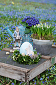 Wreath of beech with ceramic egg, quail egg, and rabbit figurine, behind it grape hyacinths and primroses