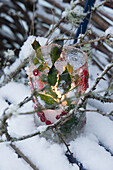 Ice lantern in the snow, with holly berries, between branches covered with lichen