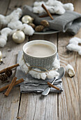Eine Tasse Milchkaffee, dekoriert mit Kranz aus Baumwolle, Serviette, Zimt und Lärchenzapfen