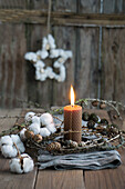Candle made of beeswax with a wreath of larch cones and cotton on linen cloth