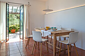 Rustic wooden dining table with white chairs in a Mediterranean room with terracotta tiled floor