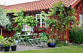 Gravel terrace with an outdoor dining area and various plants in front of red-brown Swedish house