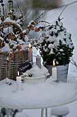 Winterdekoration mit Kerzen auf einem eingeschneiten Gartentisch