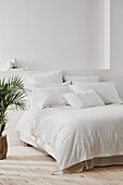 A coastal style bedroom with white walls, white bedding and a potted palm.
