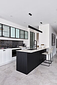 A modern monochromatic kitchen with a thin marble benchtop, black tapware and glass fronted cabinets.
