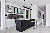 A modern open-plan kitchen with white base cabinets, wall cabinets with glass fronts and a black kitchen island