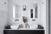 A modern double ensuite bathroom in monochromatic décor with white subway tiles, black tapware and black joinery.