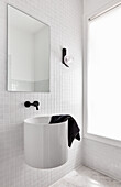 A modern white bathroom with white subway tiles, a round hanging basin and balck fittings