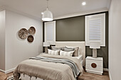 A coastal style bedroom with beige linen bedding, an olive feature wall and woven ethnic baskets on the wall.