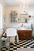 Freestanding bathtub and rustic vanity in a bathroom with checkerboard tiles and white wood paneling
