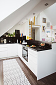 Open plan kitchen with white cabinet fronts in an attic apartment, woman in background
