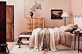 Double bed with headboard, pillows and blankets, floor lamp, landscape painting and chest of drawers