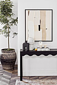 Dark console with vases, modern art on the wall and a small tree in a pot
