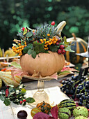 Ausgehöhlter Kürbis mit Herbststrauß auf Gartentisch