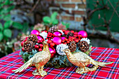 Zwei goldene Fasanen vor weihnachtlicher Kranz auf rot karierter Tischdecke