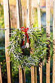 Christmas wreath with red bow hanging on a chestnut paling fence