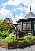 Schwarz gestrichener Pavillon und kleiner Beet mit rostigem Zaun
