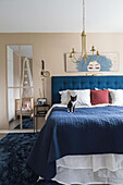 Blue bed with blue bedspread and cat in light bedroom in beige tones